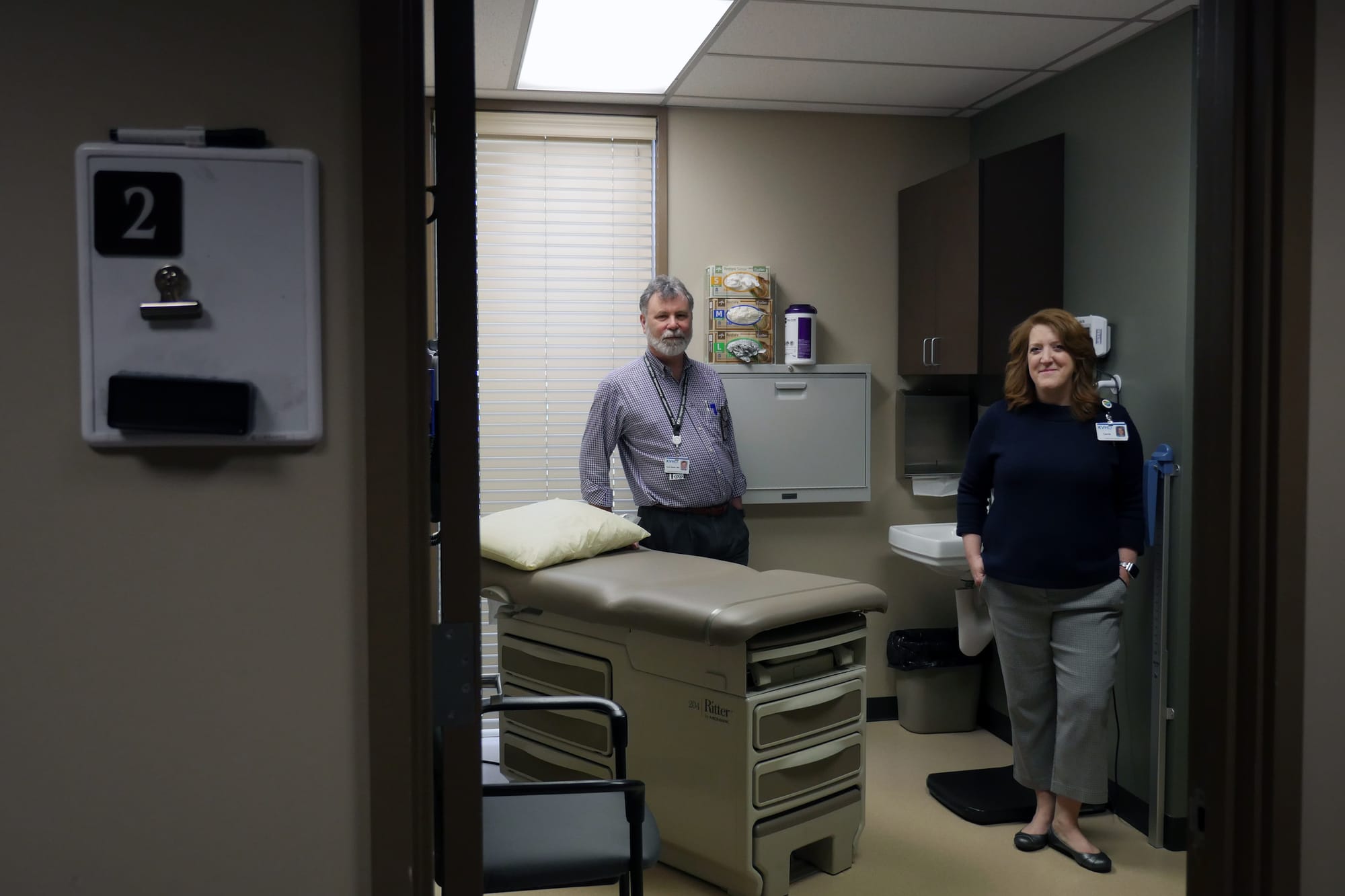 Two medical staff stand inside exam room