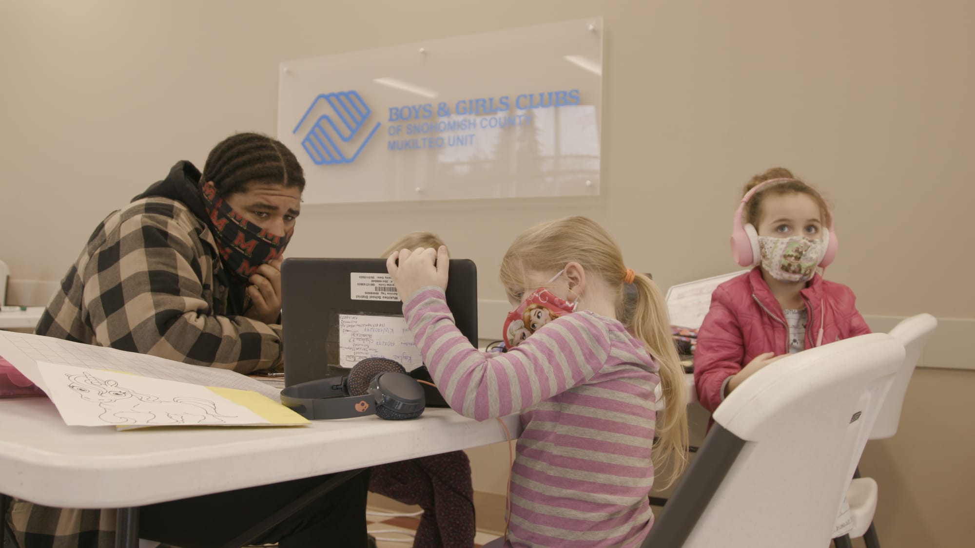 A teacher helps two students wearing COVID masks