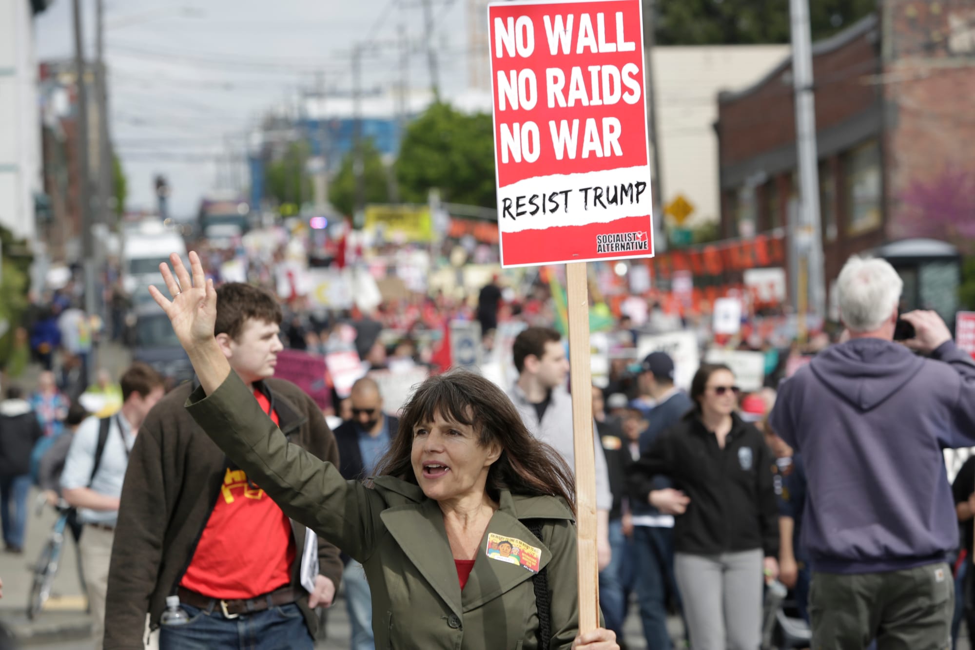 Preschool teacher Lauren Tozzi of Seattle, who says she never misses a march, waves to onlookers during the annual May Day March for Workers and Immigrant Rights in Seattle, May 1, 2018. (Jason Redmond for Crosscut) 