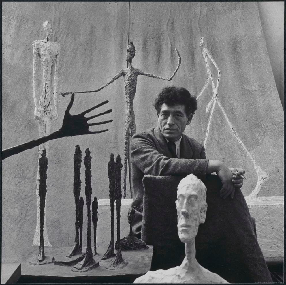 An artist in his studio, black and white photo featuring his slender artworks in metal and plaster