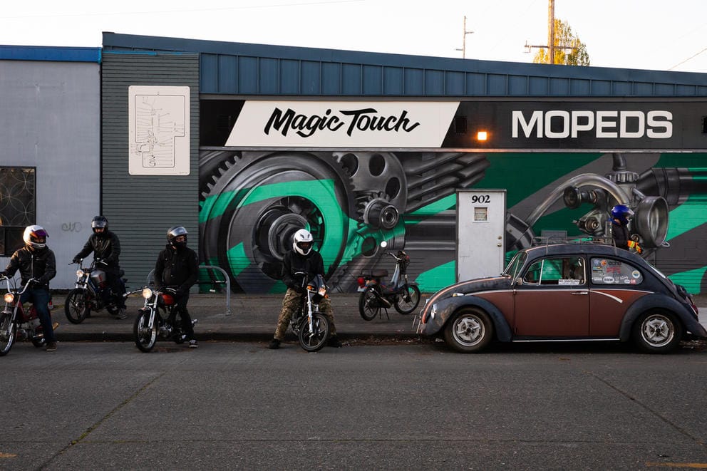 Mopeds and riders and a VW Bug car. 