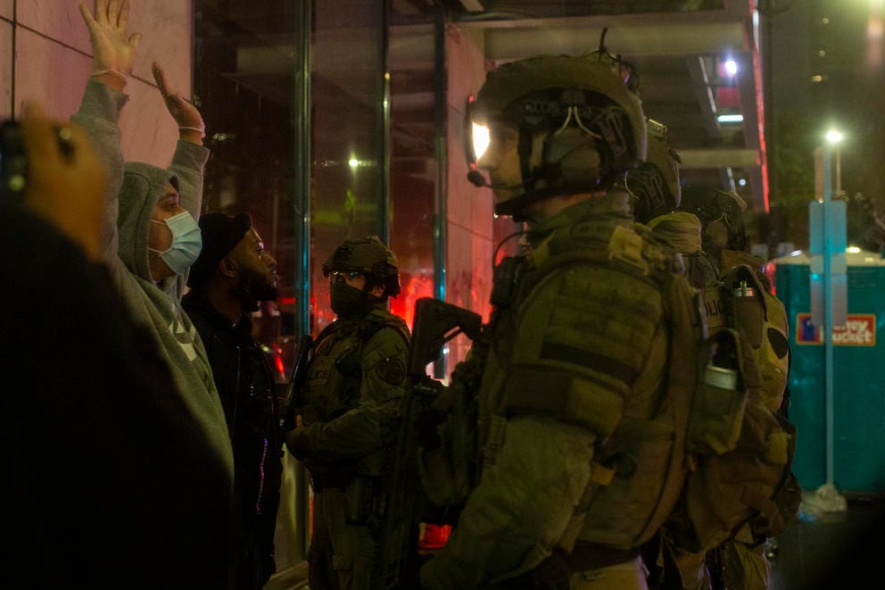 Police talk to a demonstrator who has their arms up 