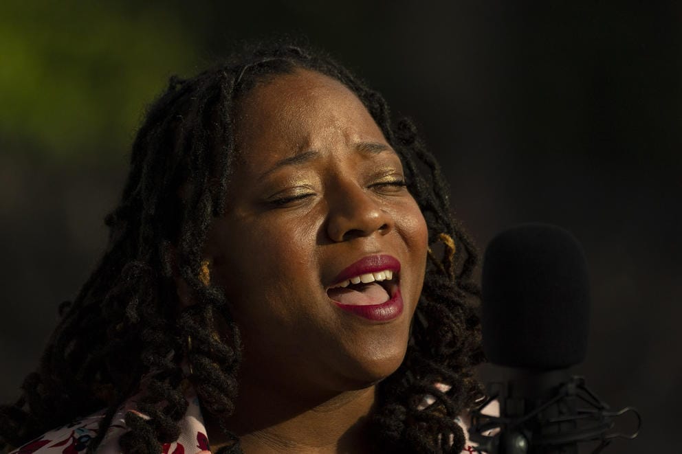 Person with eyes closed, sunlight on her face, mouth open because she is singing (