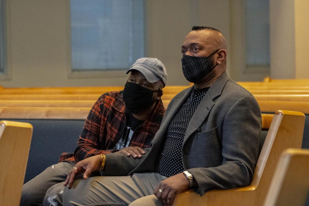 Two people, sitting on pews in church, masked, one of them holding the other's arm, eyes smiling and in anticipation.