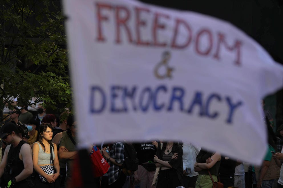a woman is lit up in the sun, a flag with the words Freedom & Democracy flies in the foreground