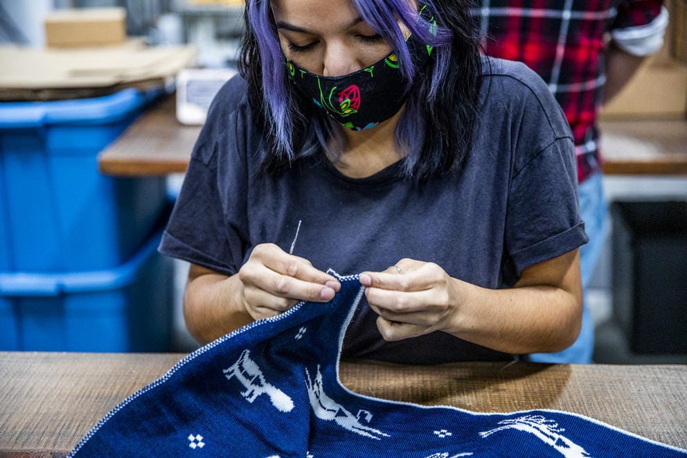 Person with mask and in dark gray t-shirt takes small clippers to the edge of a blue and white woolen blanket