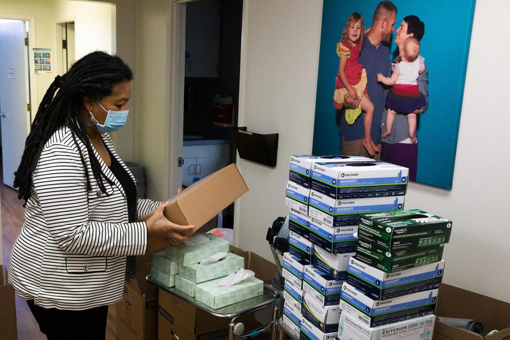 Sharon Dudash holds a box, standing in front of a other supplies that are neatly stacked