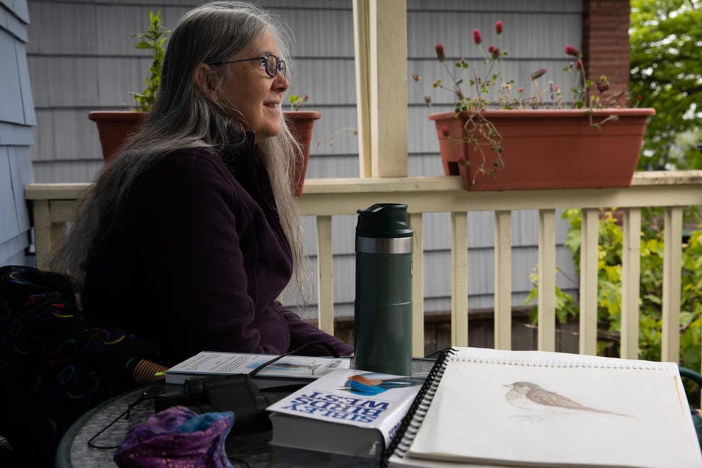 a woman on a porch looks out at a backyard with sketchbooks in the foreground