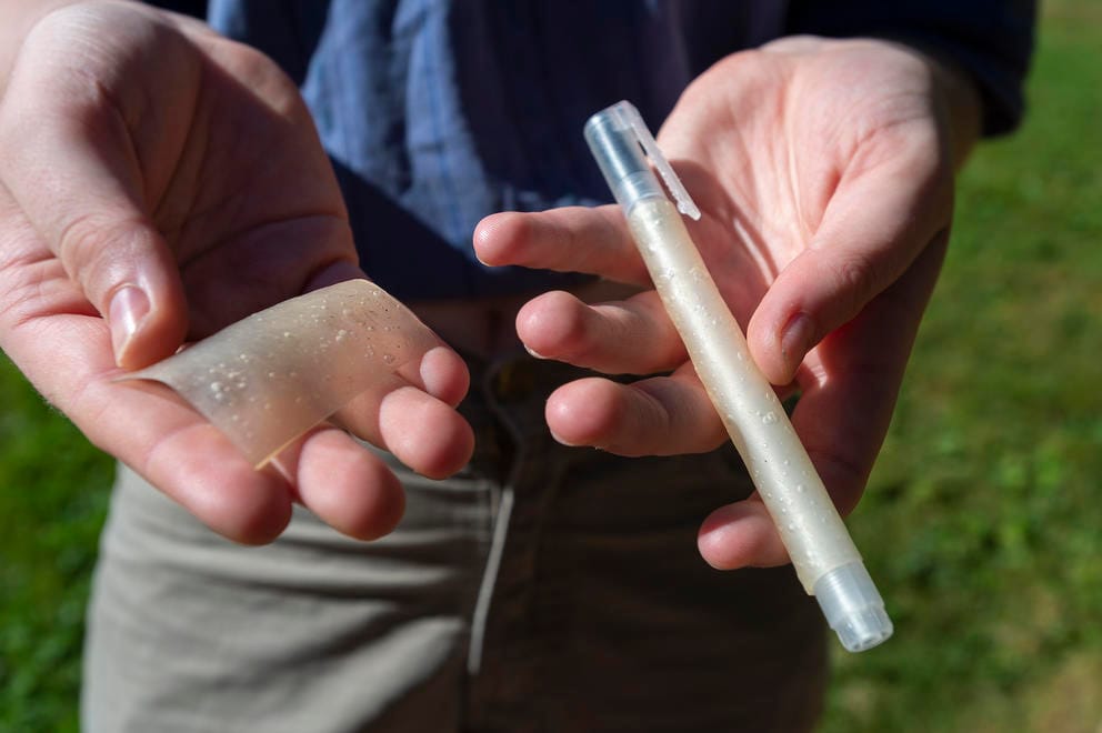 A person's hands holding a piece of bioplastic and a pen casing made out of the material