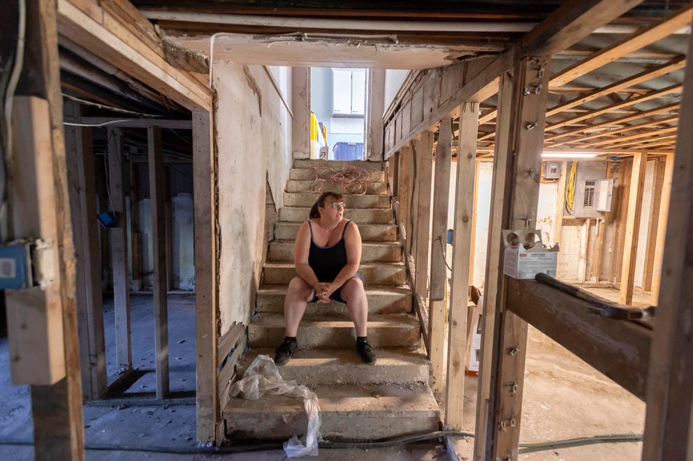 A woman sits on stairs leading down to her basement