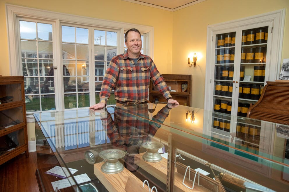 John Larson rests his hands on a glass display case of museum artifacts.