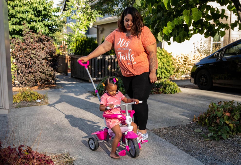 a mother pushes her young daughter on a tricycle