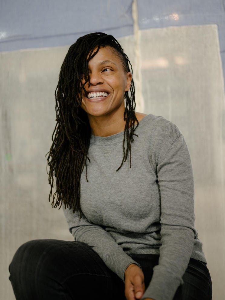 Person, who is Black, in grey sweater looks away from camera and laughs