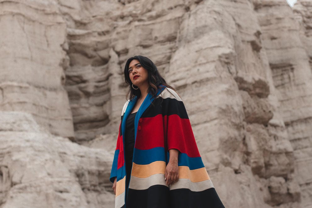 A woman in a long, striped cardigan stands in front of a large rock formation