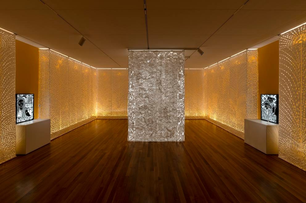 A pillar of paper scrolls cut with symbols in a room clad with intricately cut paper, glowing with a backlit goldon glow
