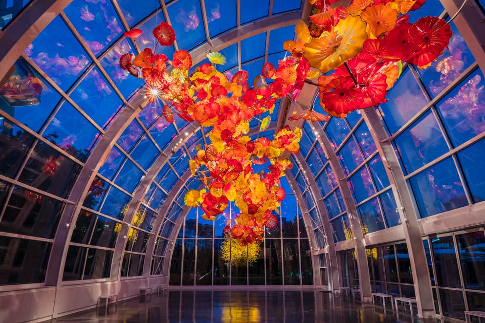 a glass building with a huge orange and red glass sculpture hanging from the ceiling, with the night sky visible behind