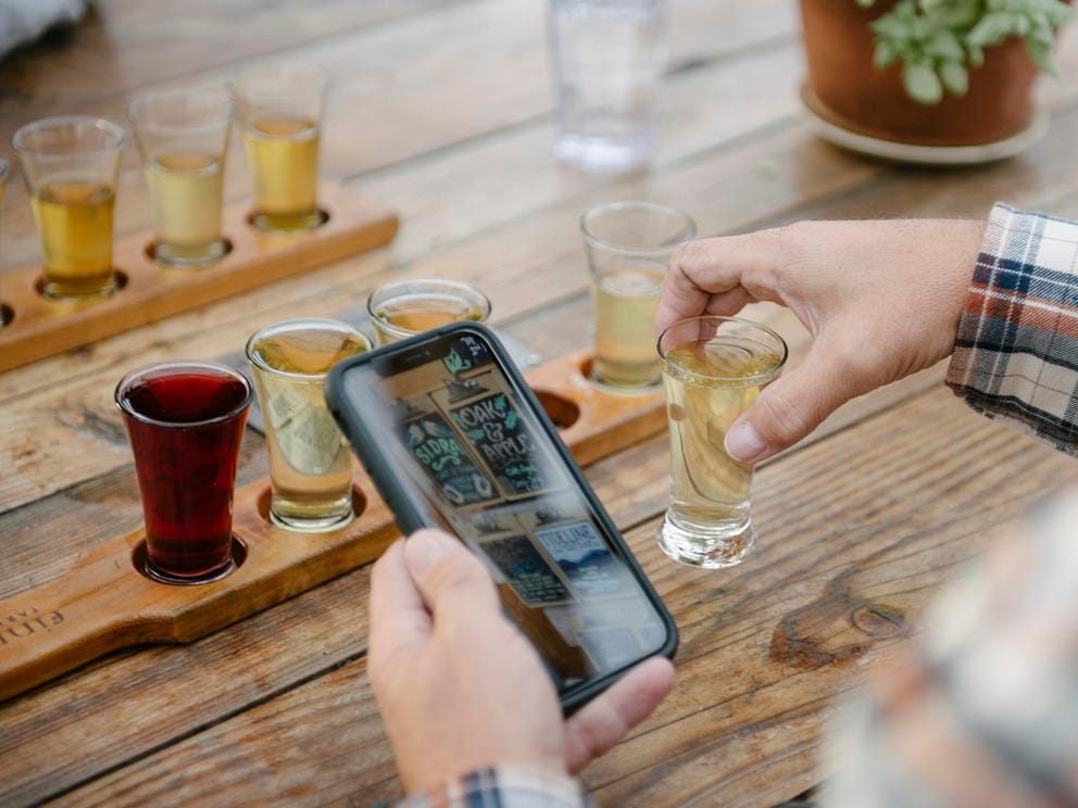 someone holding a phone above a table near a flight of ciders