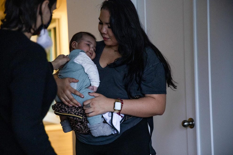 A woman holding an infant talks to another woman