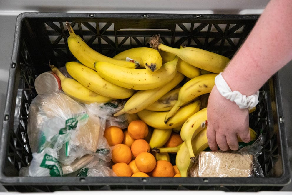 A hand reaches into a box full of bananas and oranges.