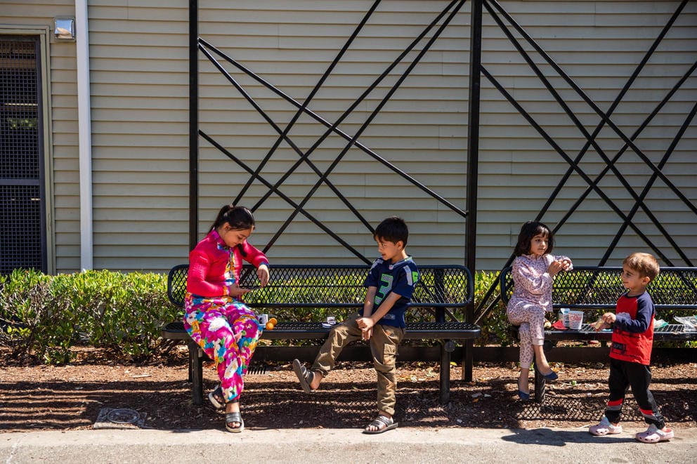 Four children relax on a park bench after eating their lunches.