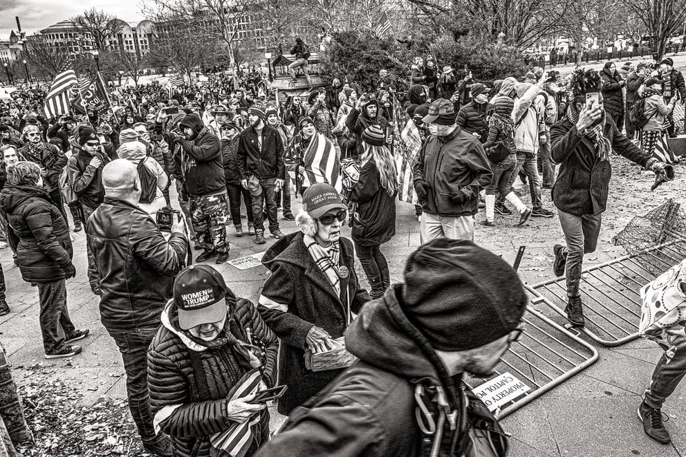 People walk over a fence, one woman wearing earmuffs, another a shopping bag, in a black and white photo