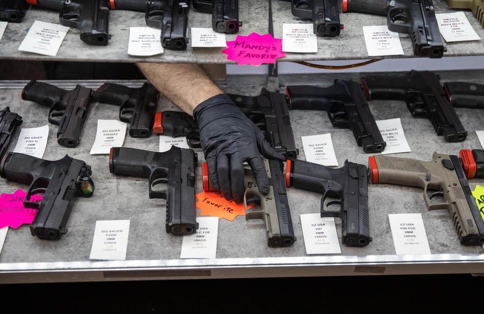 Employee with gloved hand returns handgun to display case