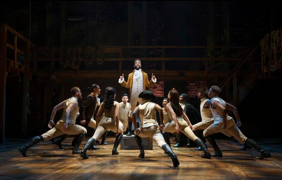 Person on stage in beige clothing surrounded by people