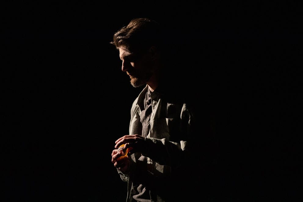 white person faces to the left in a dark black void, he is lit sparsely from the side