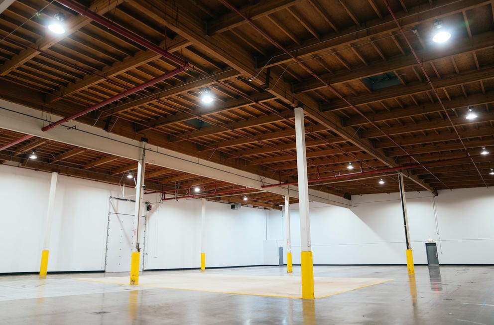Large room with tall ceilings and some beams, featuring a plywood floor in the middle