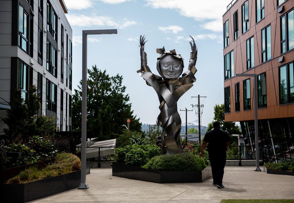 metal sculpture made out of a twisted bouquet of metal panels and round head, arms raised.