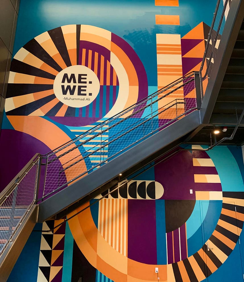 a two-story mural featuring turquoise and orange swirling stripes that reads Me, We