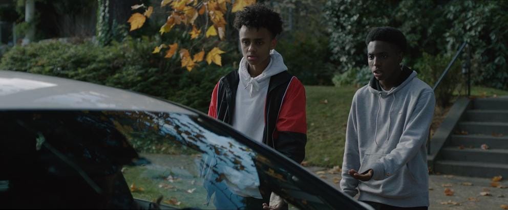 Two teens face a car with open window
