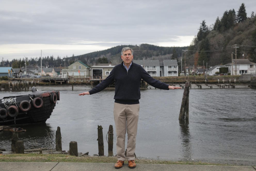 A man stands with his back to a river, his hands are raised just above waist level on either side