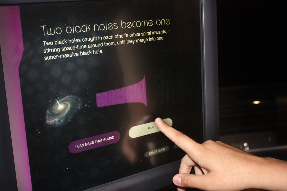A computer screen depicts a black hole. The screen reads: