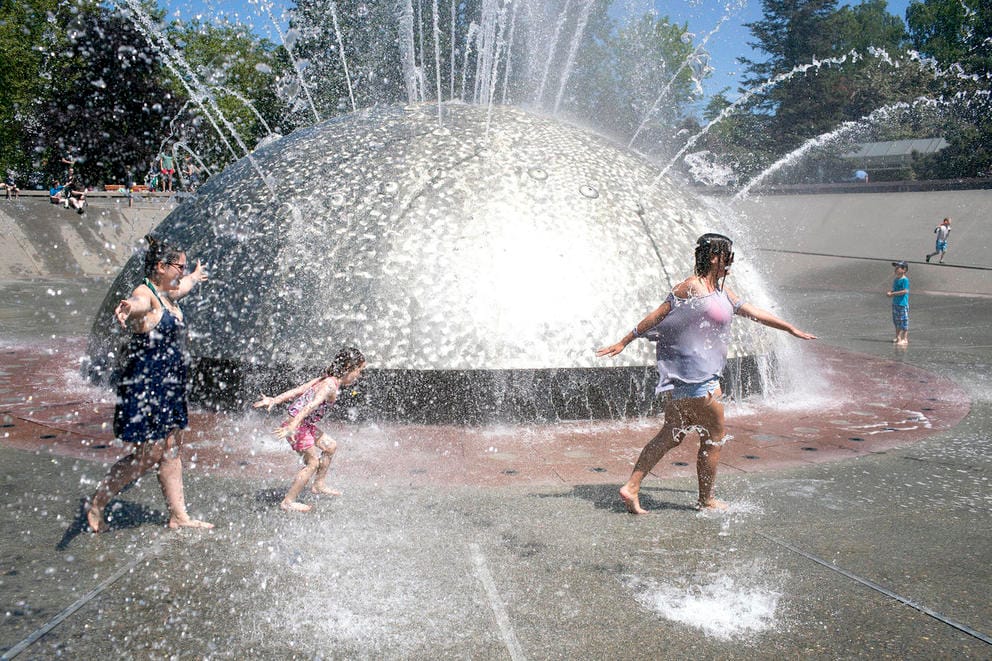 three people run through a fountain as water sprays