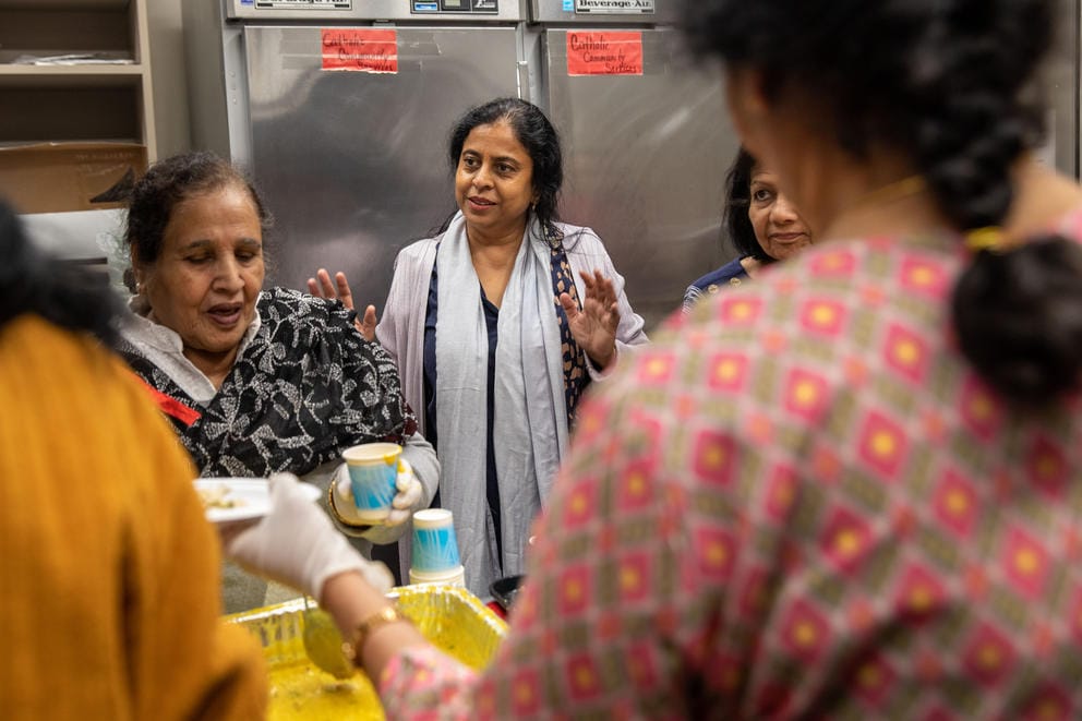Uppala stands in a stainless steel commercial kitchen surrounded by people preparing food.