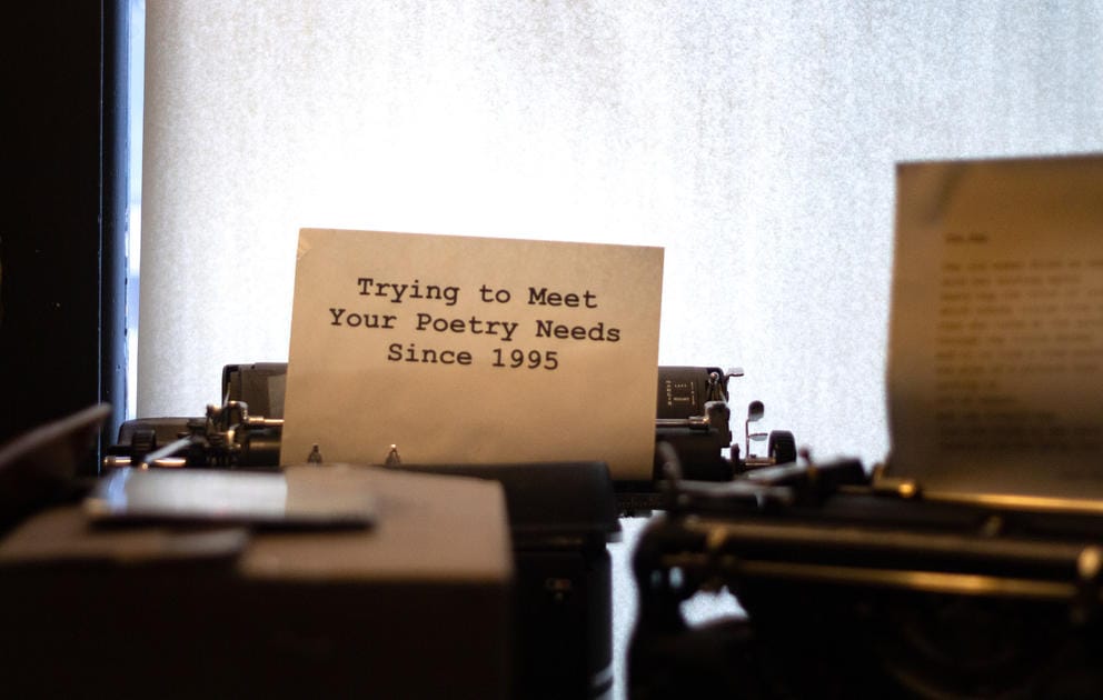 Antique black typewriter with white page and black font, reading: “Trying to meet your poetry needs since 1995”