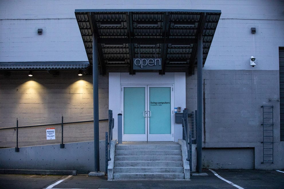 facade of a gray building, an unlit neon sign on the awnung says: