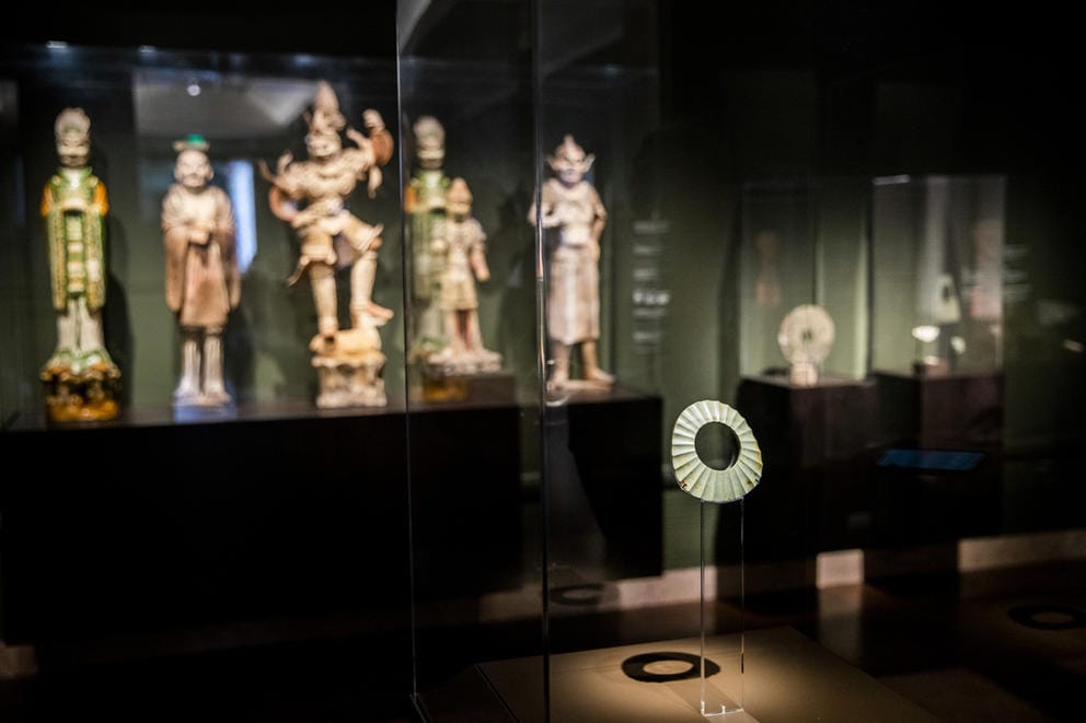 Darkened museum gallery room with spotlighted figures as well as a jade-colored wheel-shaped stone on a pedestal
