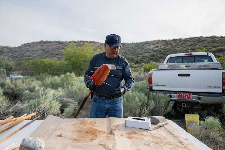 A man holds a skewered salmon fillet at an outdoor prep station in front of a pickup truck