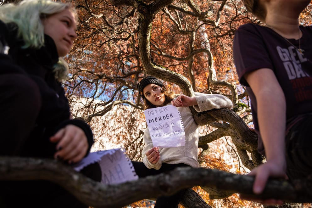 A student leaning against a tree holds a sign saying
