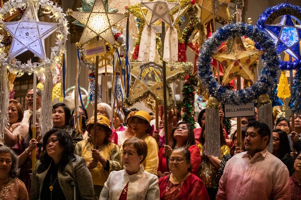 a crowd of people hold glowing star-shaped lanterns on poles up above their heads