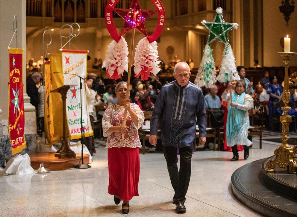 A man and a woman walk through a church side by side, the woman holds a colorful lantern on a pole