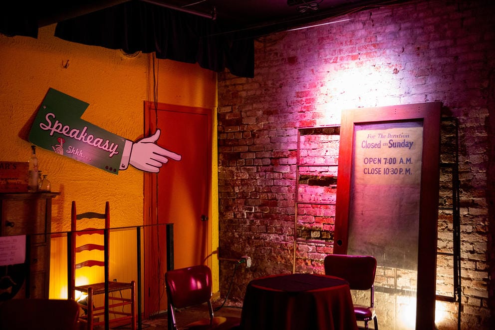 A two-seat table in the corner of the theatre. A sign in the shape of an arm pointing to the right reads
