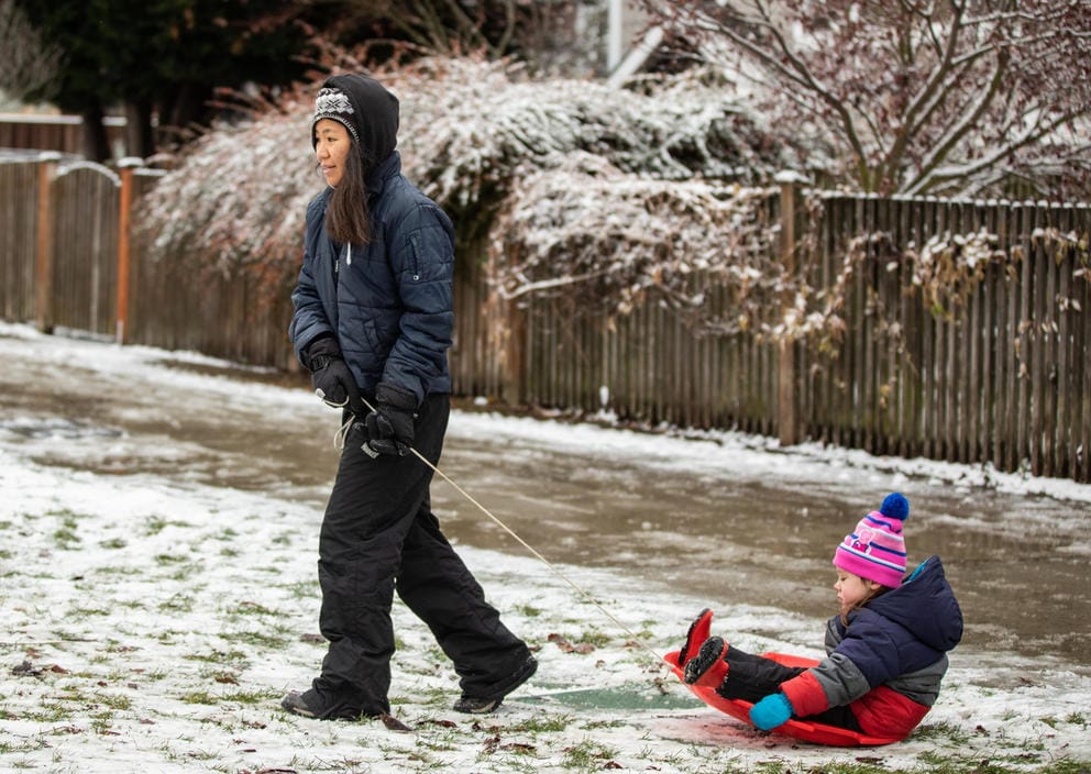 A person pulls a child on a round sled