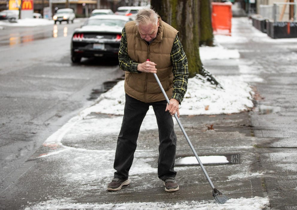A man in a puffer jack sweeping the driveway