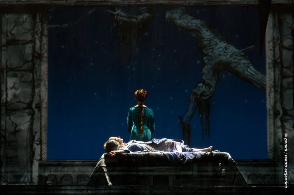 Dark stage with person lying down and one person with back turned in blue dress