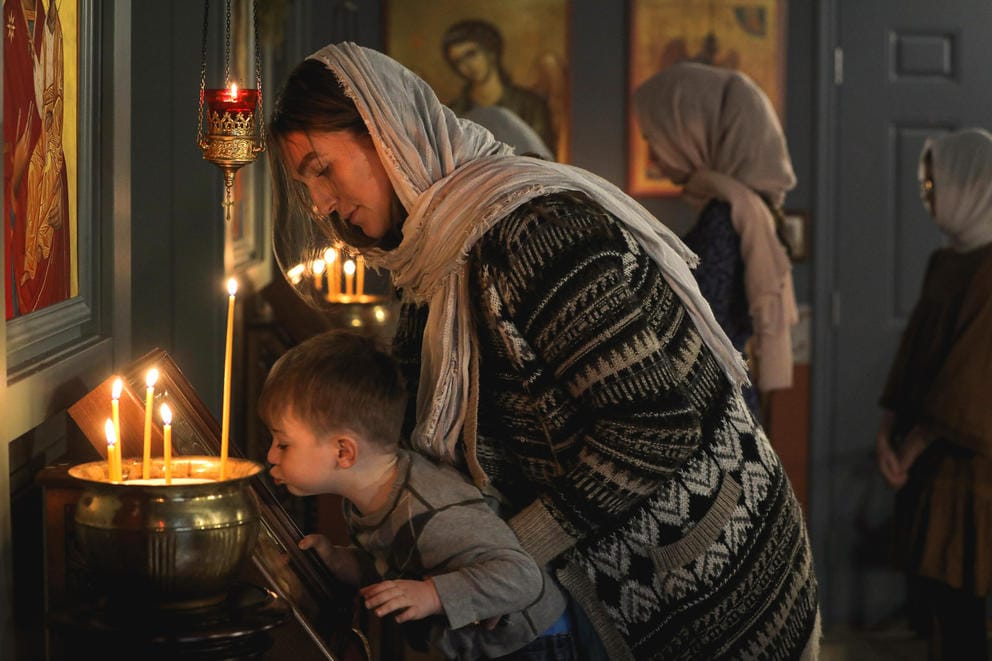 Rachel Mullins lifts her son Elijah up to kiss an icon in a darkened church lit by candles