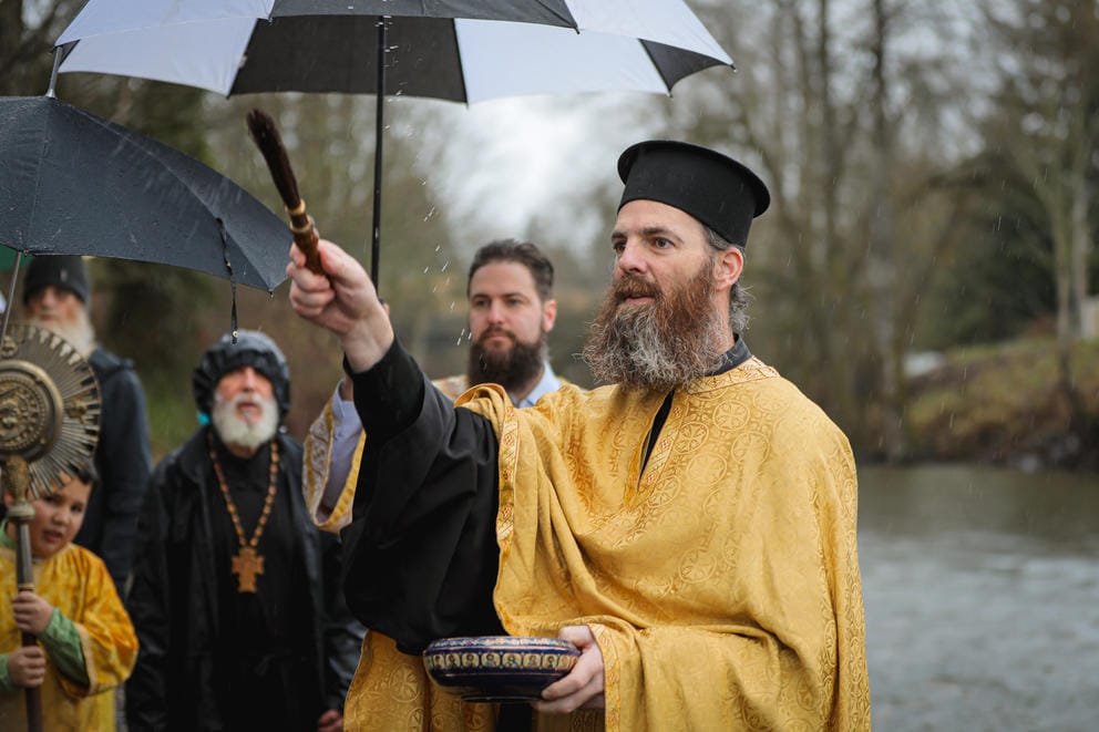 A close up of Father Sommer sprinkling holy water on members of the congregation outside