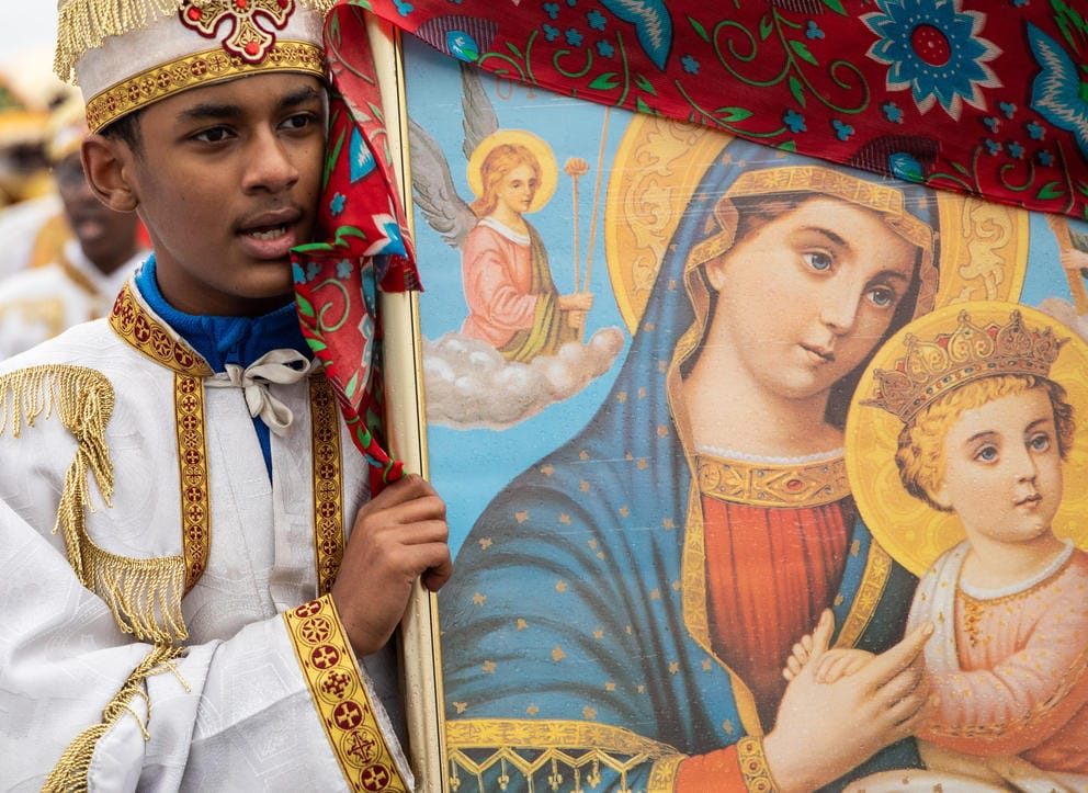 A young altar boy holds a painting of Mary and baby Jesus